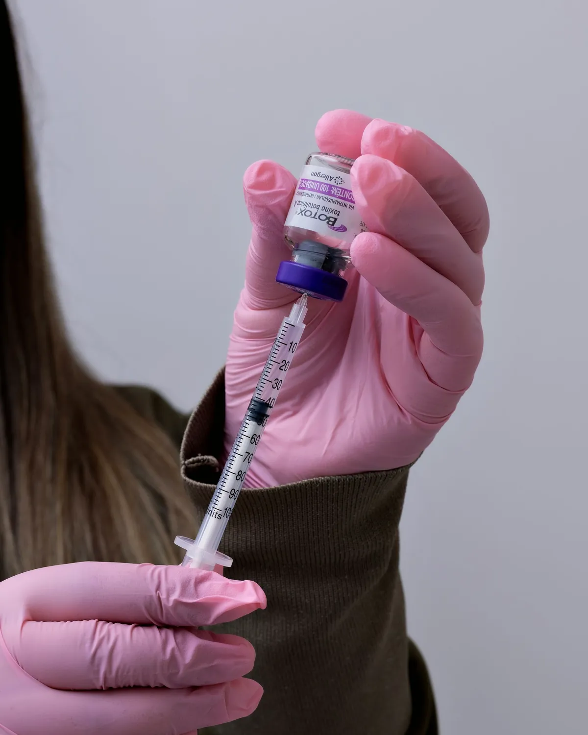 Gloved hands drawing a syringe from a Botox vial
