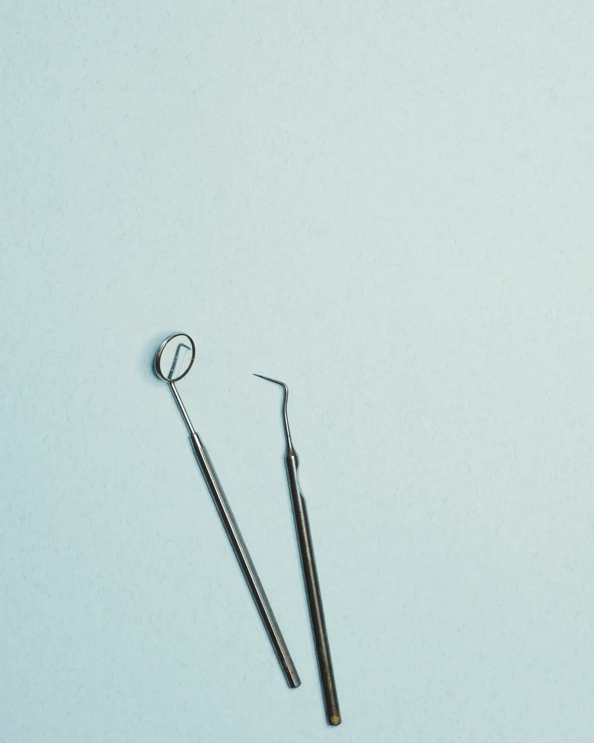 Two stainless steel dental instruments on a pale blue surface
