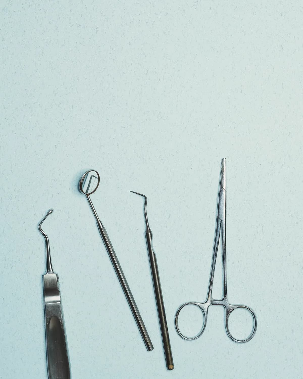 Dental scaler, mirror, probe and forceps laid out on a pale blue surface