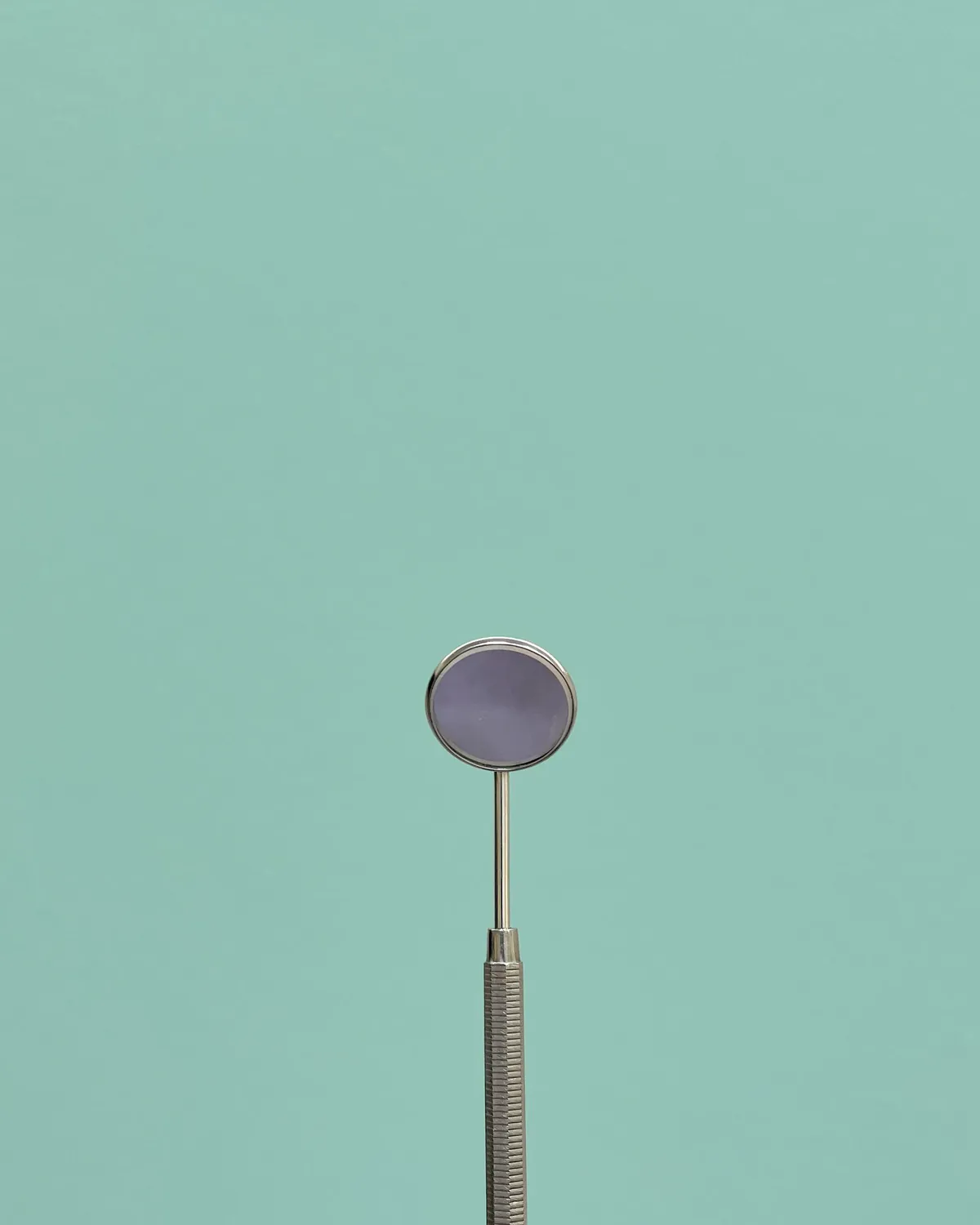 A dental mirror standing against a soft teal background