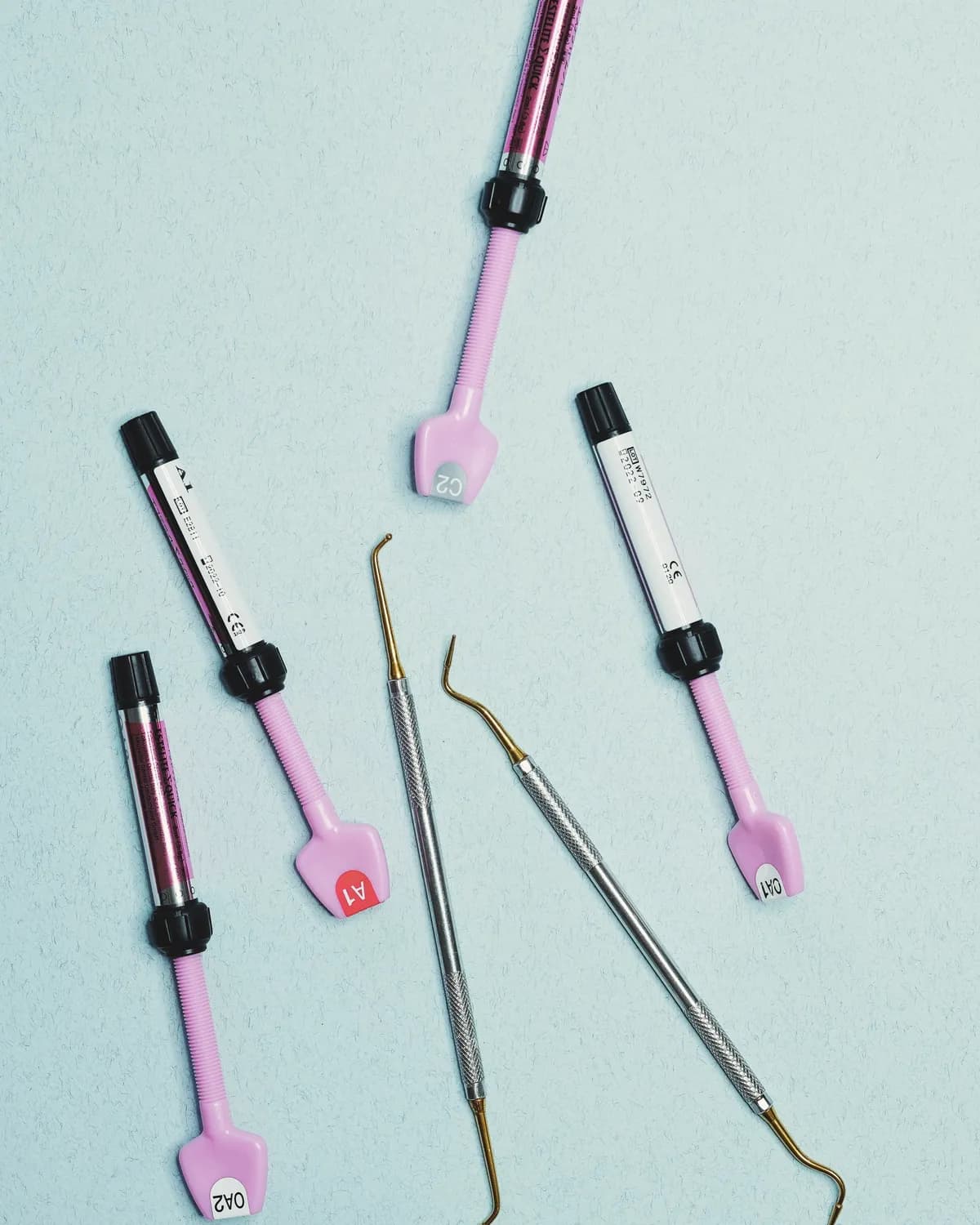 Tooth-coloured filling material syringes and dental instruments on a pale blue surface