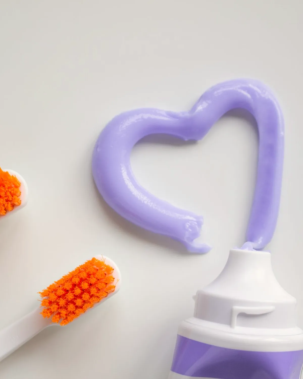 Orange children's toothbrushes beside toothpaste squeezed into a heart