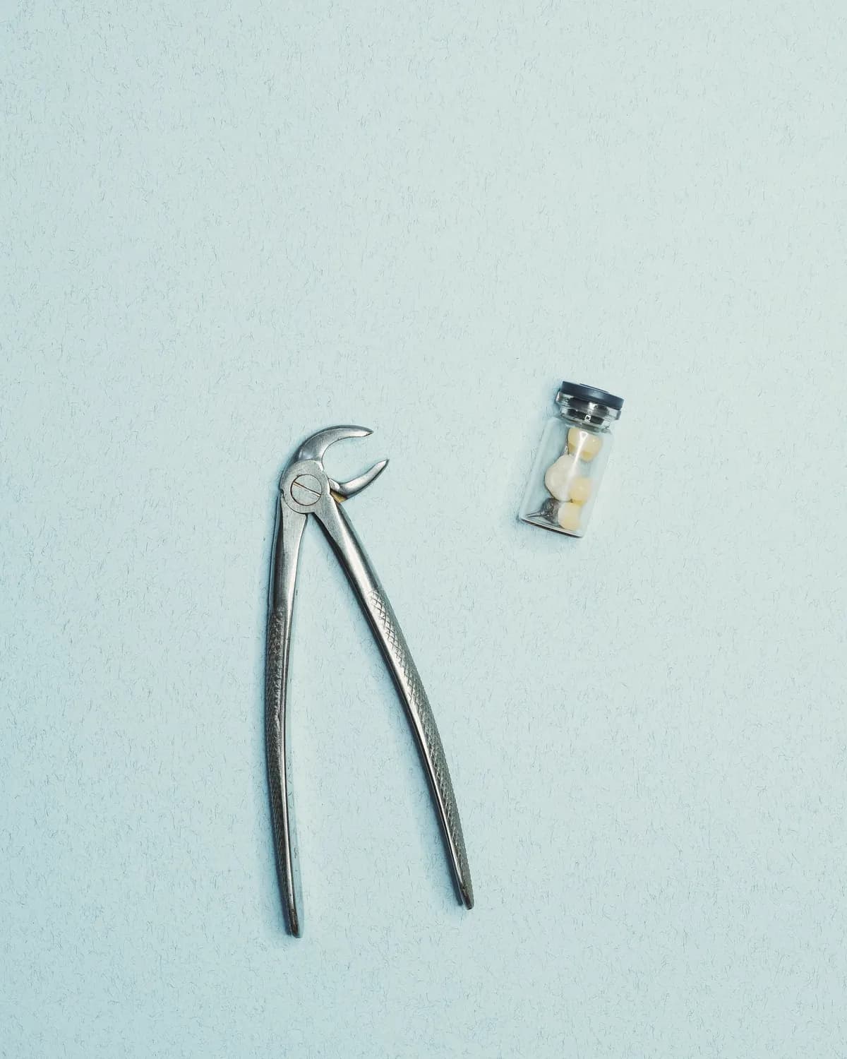 Dental forceps and a small sample tube on a pale blue surface
